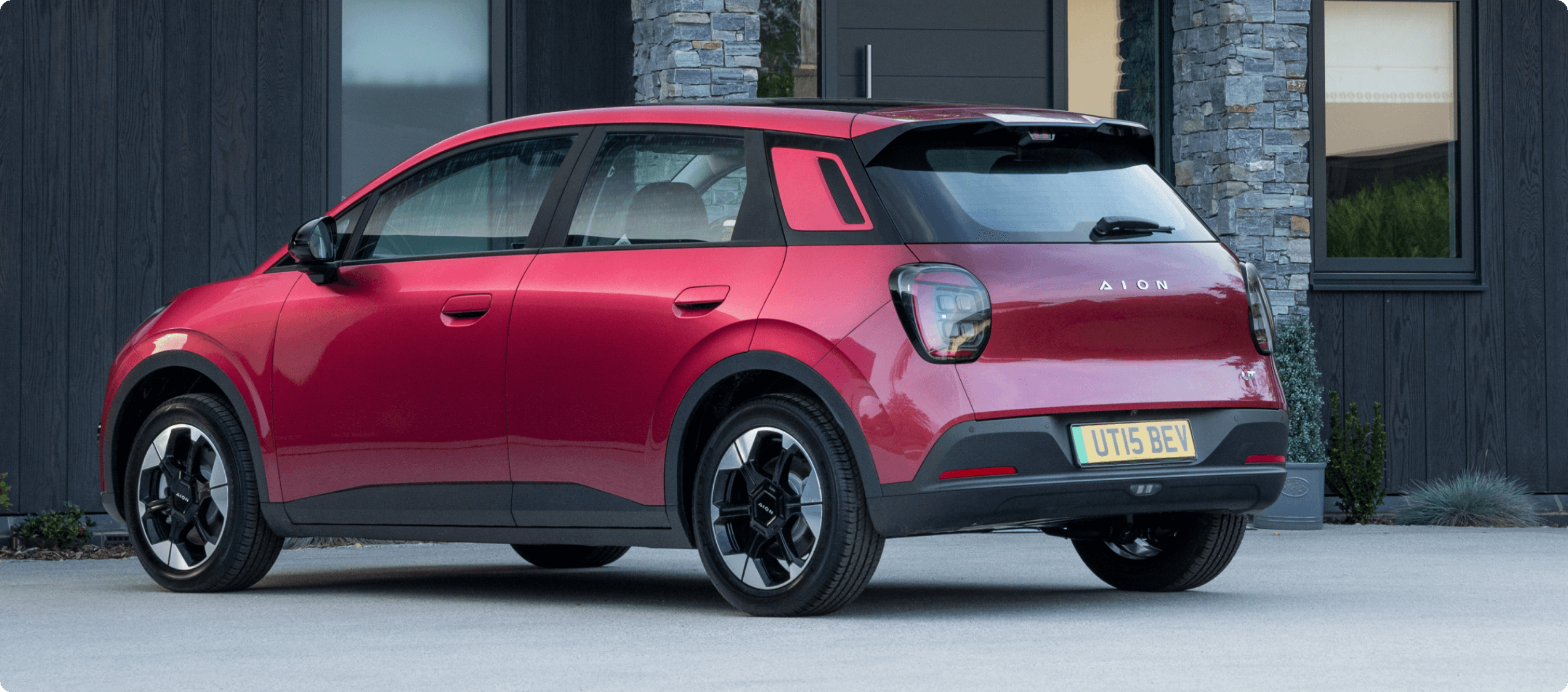 Rear three-quarter view of the AION UT electric car parked outside a modern home
