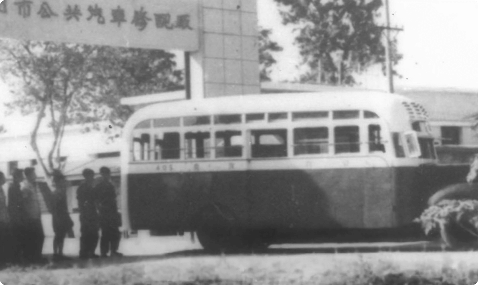 Historic black-and-white photograph of an early public transport bus outside a factory entrance