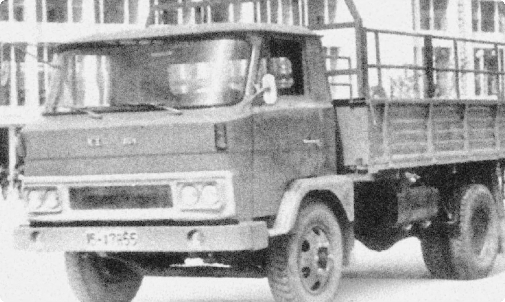 Historic black-and-white image of an early flatbed truck used for commercial transport