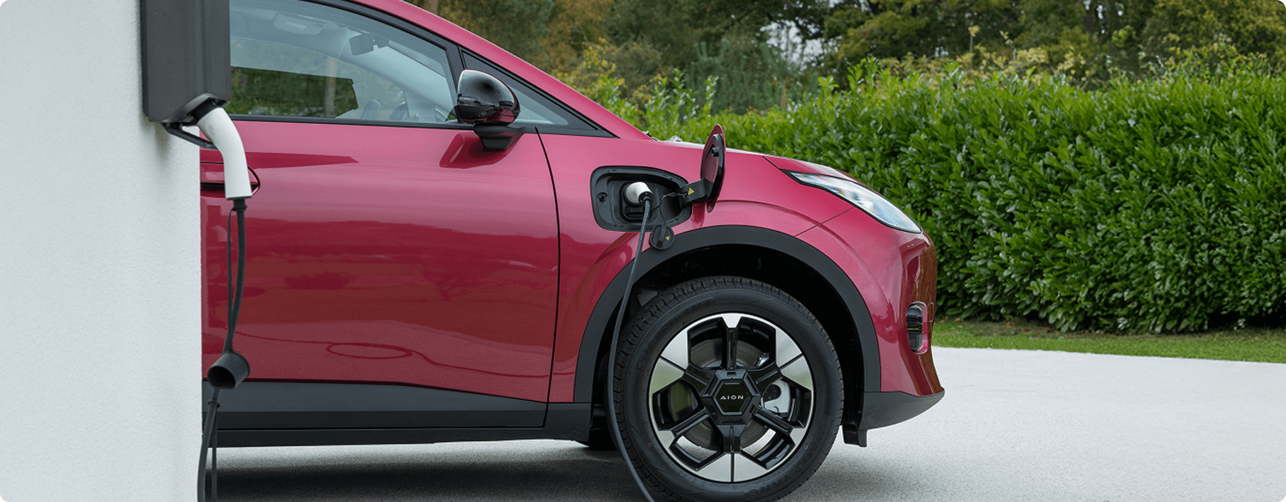 AION UT plugged into a wall-mounted home charger on a residential driveway