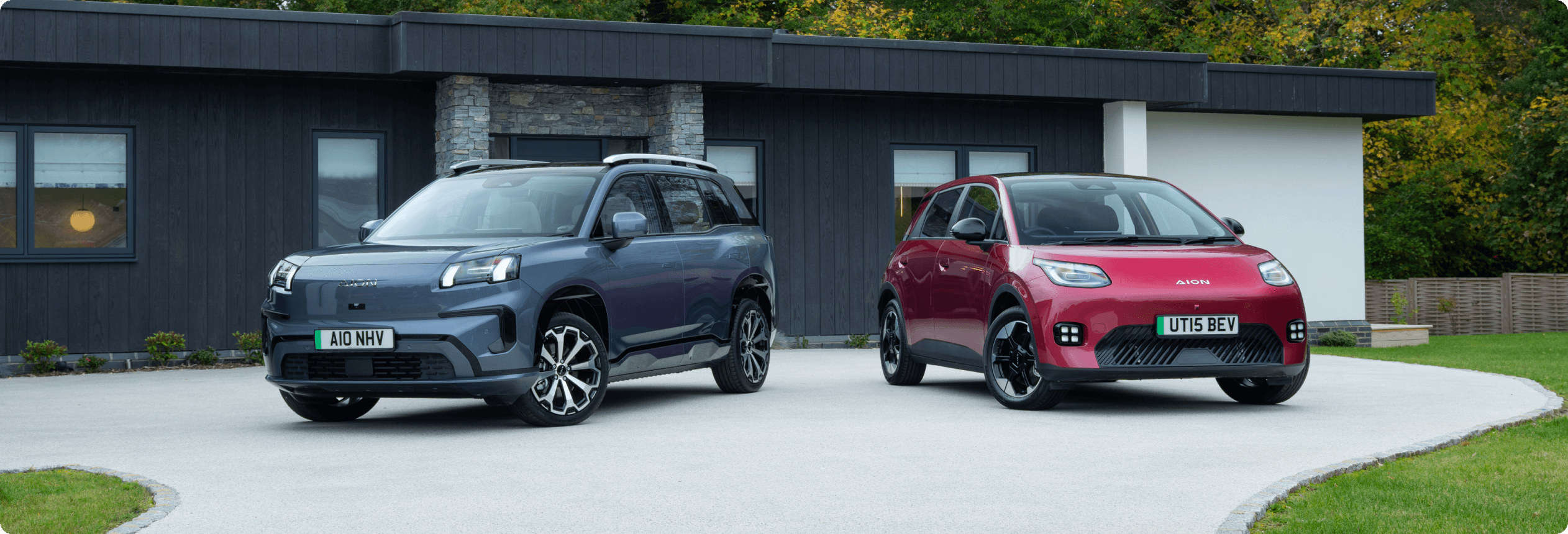 Two AION cars, a AION V and a AION UT, parked on a driveway in front of a modern house