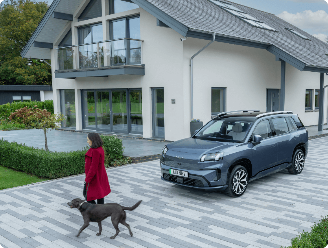 AION V parked on a modern home driveway as a woman walks a dog past the house