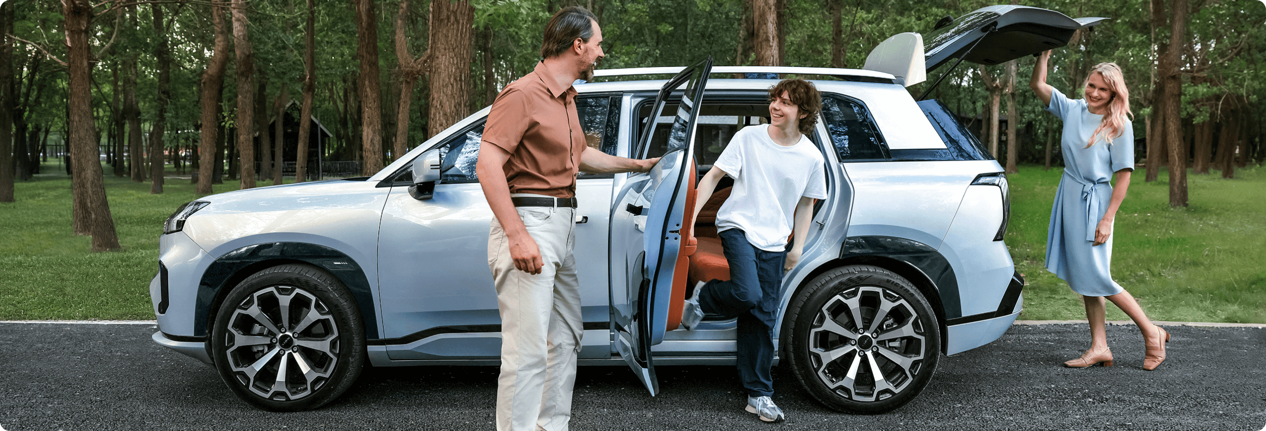 Family beside a AION V parked in a wooded park