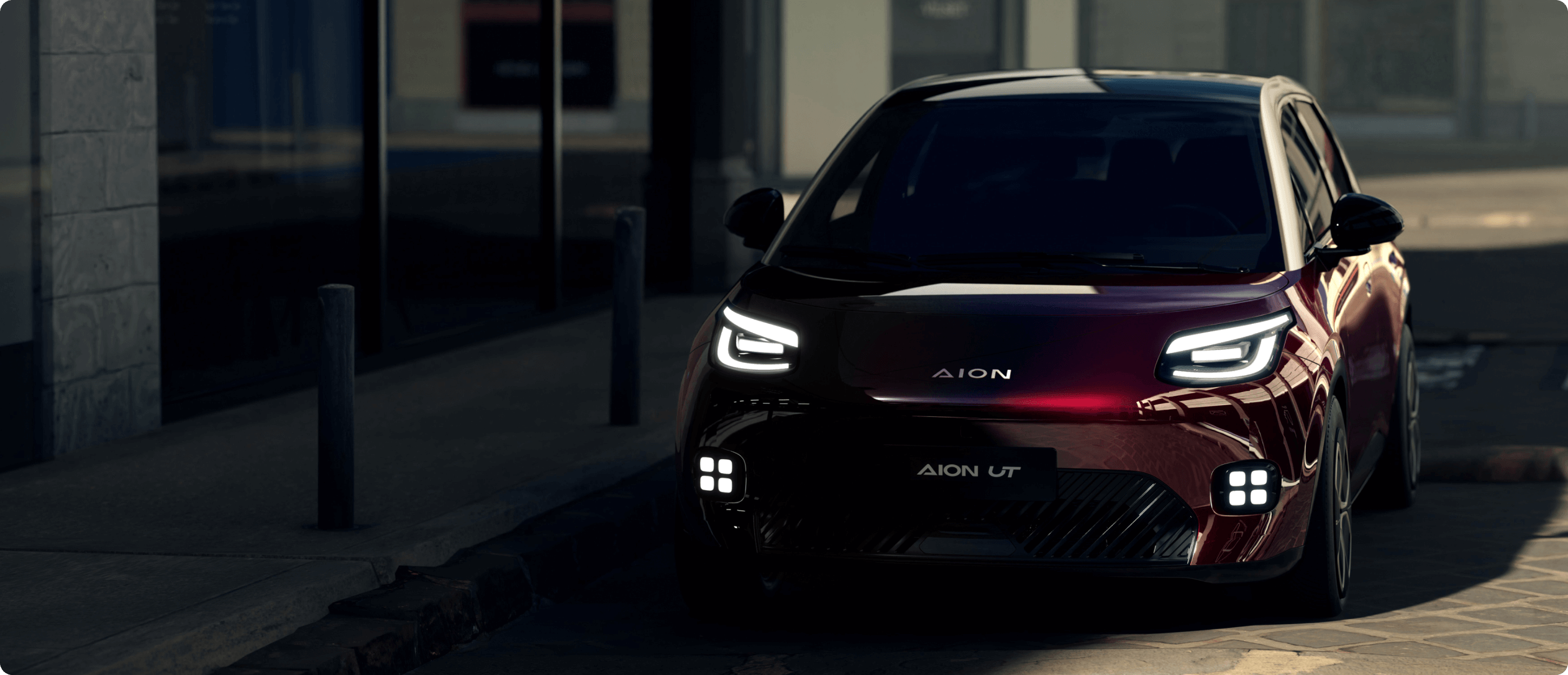 AION UT parked on a city street at night with LED headlights illuminated