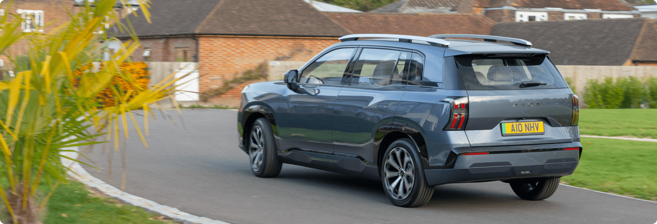 AION V driving along a residential road past brick houses