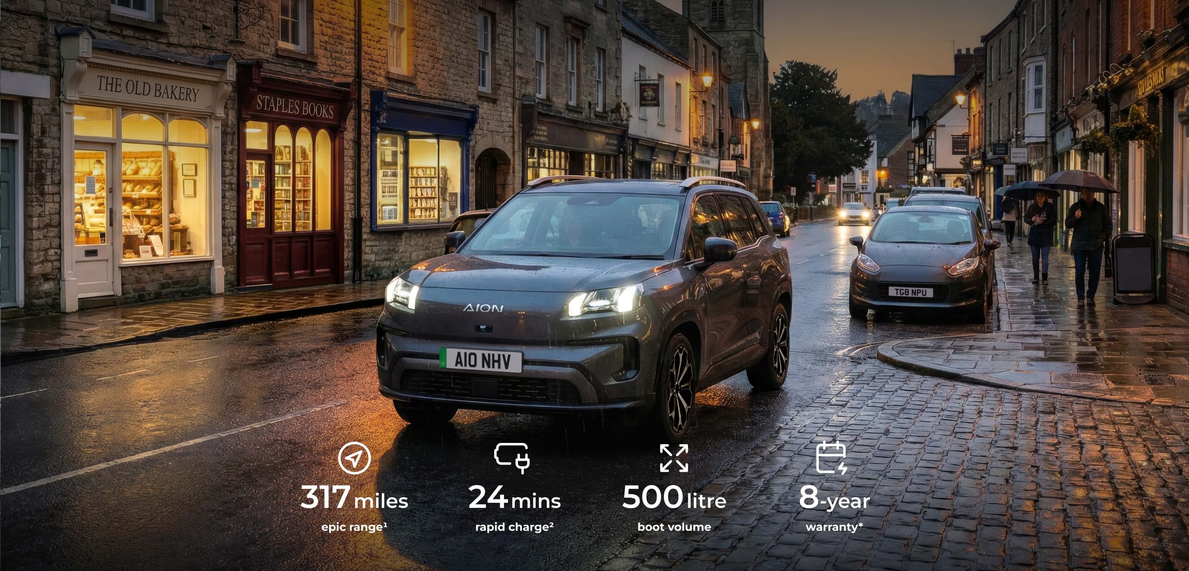 AION V driving through a town street at dusk. 317 miles epic range¹, 24 mins rapid charge², 500 litre boot volume, and 8-year warranty*.