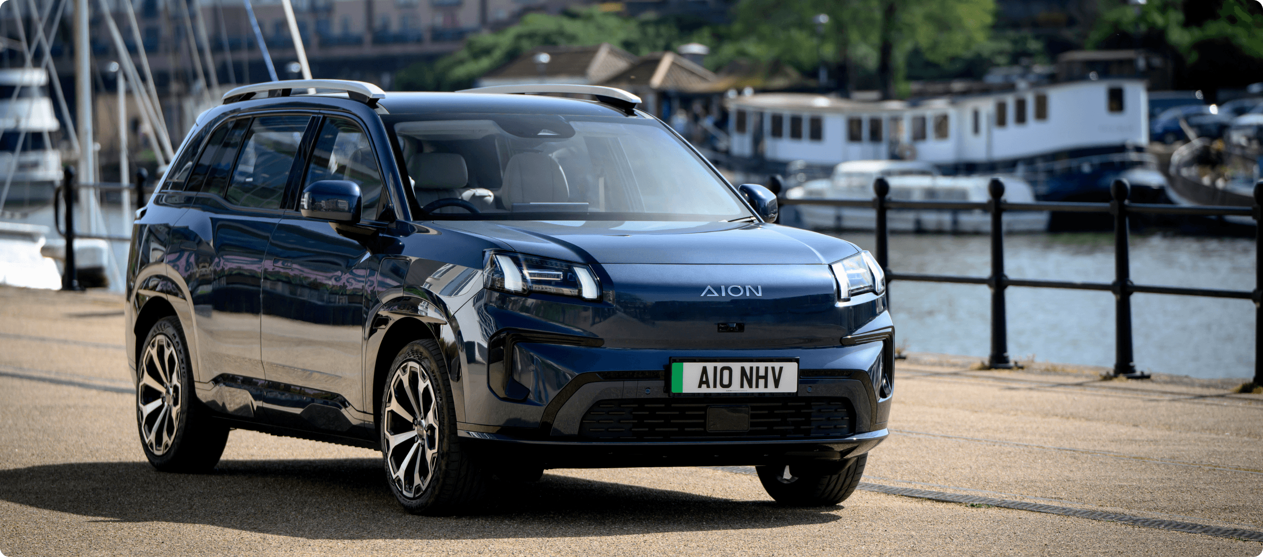 AION V parked on a waterfront promenade with boats and water in the background