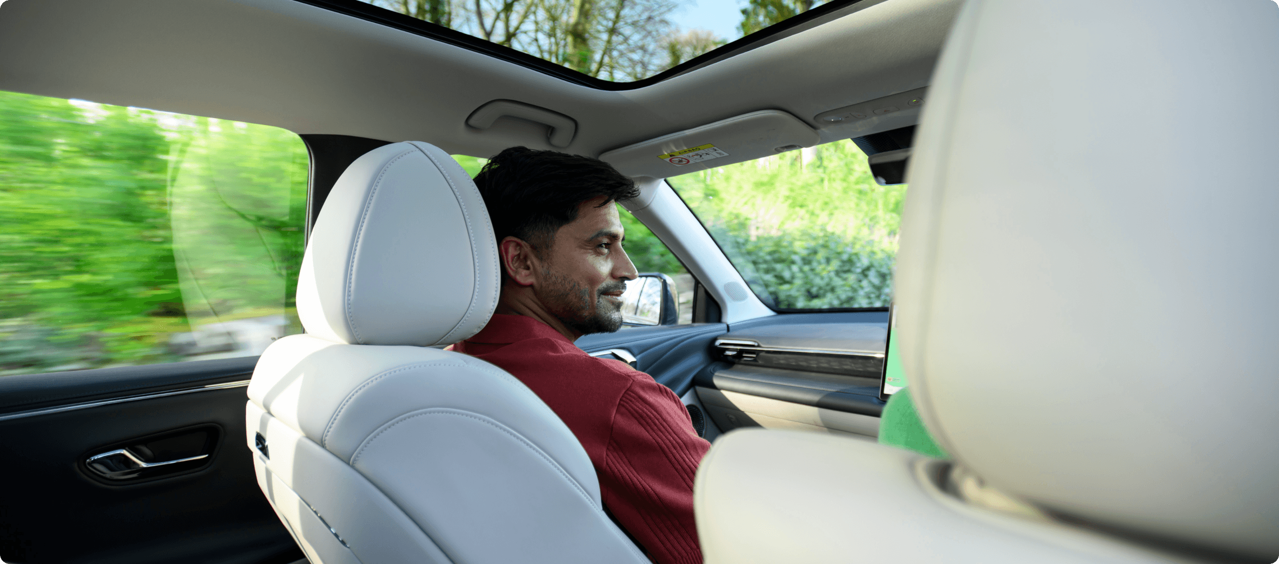 AION V interior with white leather seats and a panoramic glass roof while driving through a wooded area