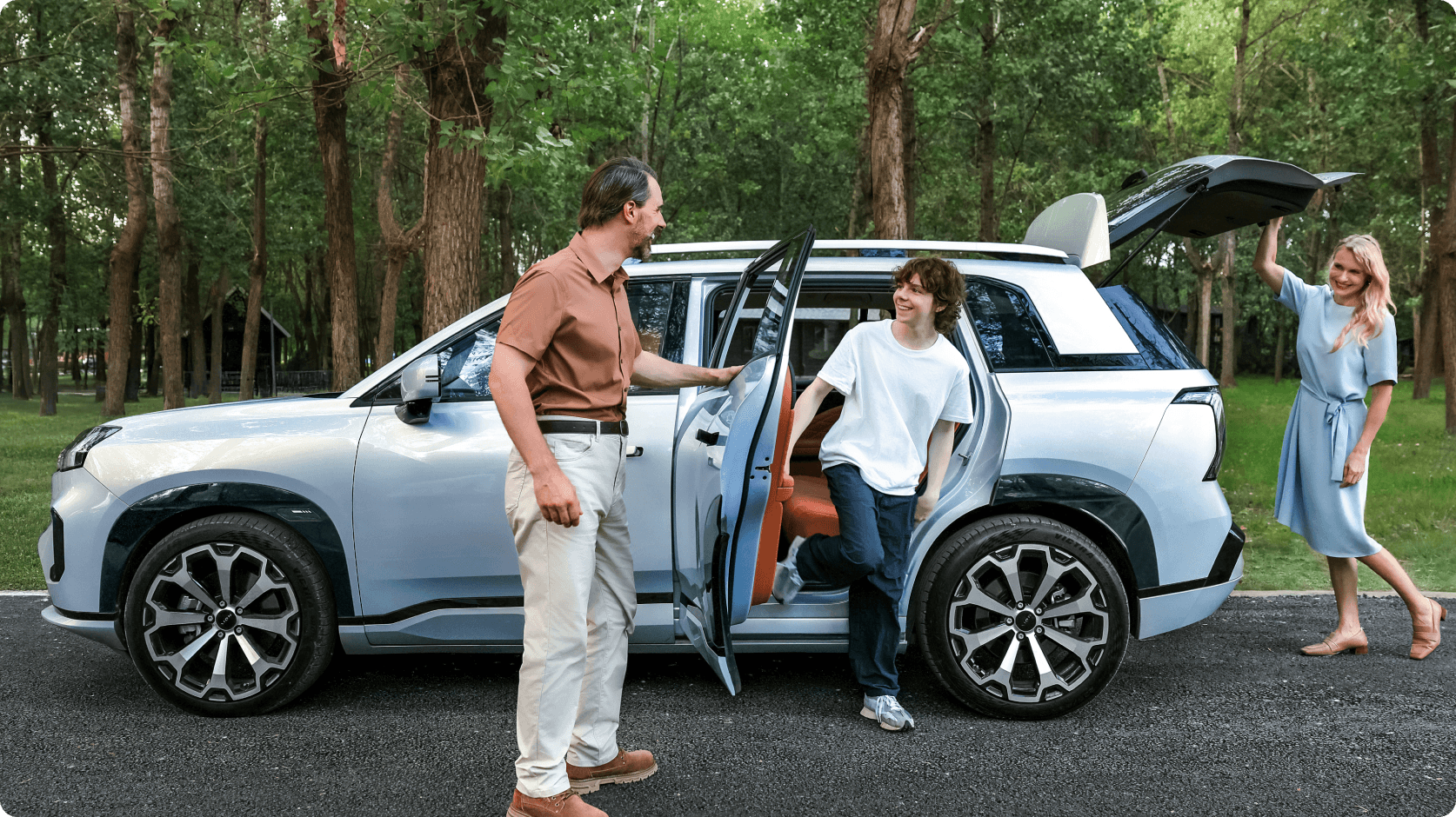 Family using the spacious interior of an AION V with the rear tailgate open in a wooded park